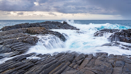 Obraz premium Powerful Ocean Wave Crashing Against Rugged Coastal Rocks in Dramatic Seascape