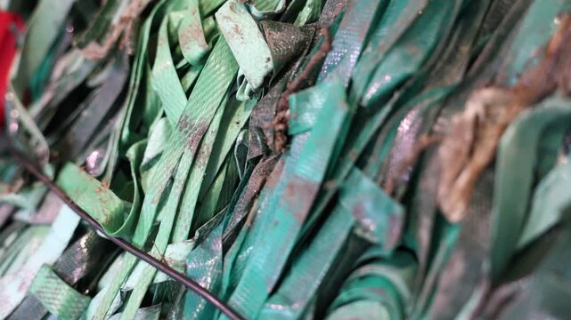 A close-up view of green plastic straps bundled together, showing dirt, wear, and texture, symbolizing industrial waste, recycling challenges, and material recovery.