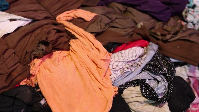 A large pile of discarded clothes and fabrics in various colors and materials, representing textile waste, recycling, and sustainable reuse initiatives