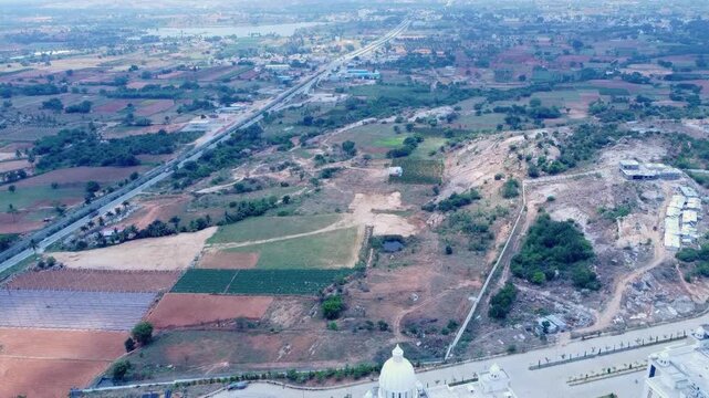 High-altitude aerial shot of the sprawling landscape around Kanha Shanti Vanam in Telangana, India. A major highway and railway line cut through patchwork farms and the arid terrain of the Deccan