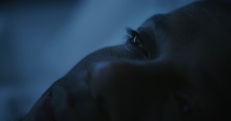 Obraz premium Close up of Man's Face Illuminated by Cold Night Light. African American Man Slowly Drifts Off Sleep After Hard Day. Concept of Insomnia, Poor Rest, Anxiety, and Sleepless Nights. Static Shot.