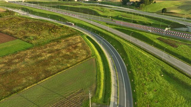 Aerial view of a modern highway interchange (S6) cutting through lush green and brown fields near Gdynia. Traffic moves along the new roads at sunrise.