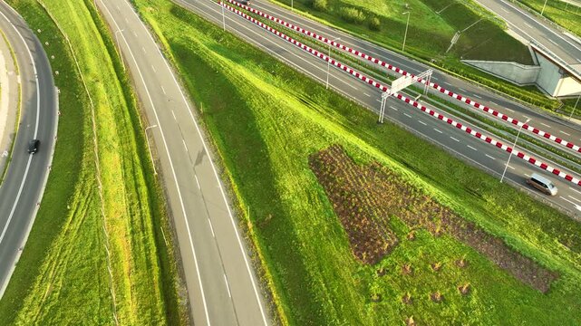 Extreme close aerial view of cars and vans driving on a multi-lane highway (S6) with distinctive red and white barriers, flanked by steep green embankments.