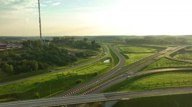 Wide aerial shot of a massive highway interchange near Gdynia featuring a communications mast on a hill, bathed in the golden glow of early morning light.