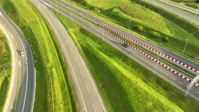 Sweeping aerial shot of the S6 expressway lanes and service roads, curving through lush green, undulating hills and embankments outside Gdynia.