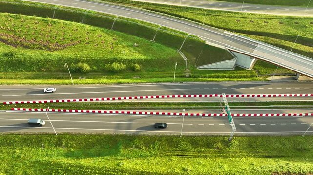 High-angle drone view of an expressway overpass near Gdynia, showing light traffic beneath the bridge and flanked by lush green grassy embankments.
