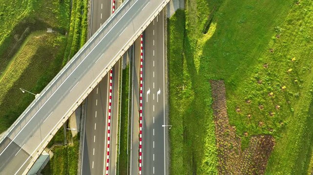 Top-down aerial shot of a white car driving under a highway overpass on the S6 expressway, highlighting the stark geometric contrast and bright green slopes