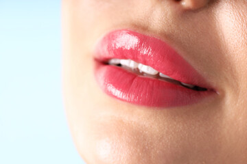 Woman with beautiful pink lipstick on her lips against light blue background, macro view