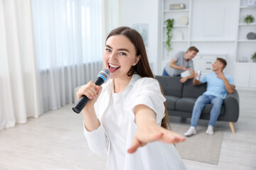 Young woman singing karaoke with friends at home, selective focus
