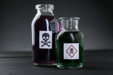 Bottles of poison with warning signs on black wooden table, closeup