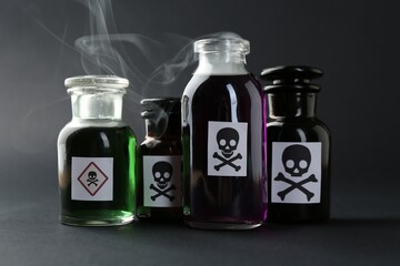 Bottles of poison with warning signs and smoke on dark background, closeup