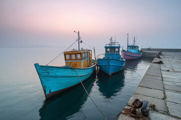 Colorful fishing boats moored at harbor on calm misty morning