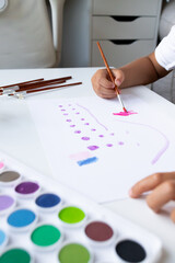 Child painting with watercolors on white paper in art studio setting