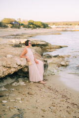 A woman in a long dress stands near the rocks on the seashore, boho style