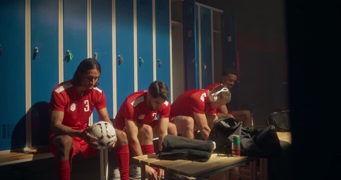 Soccer Athletes in Red Uniform Sitting on a Bench in the Locker Room, Dressing Up and Preparing for the Tournament. Footballer Listening to Music on Headphones, Teammate Playing with a Ball
