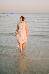 A woman in a long dress stands in the sea, summer seaside vacation