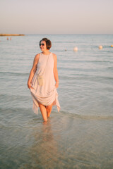 A woman in a long dress stands in the sea, summer seaside vacation