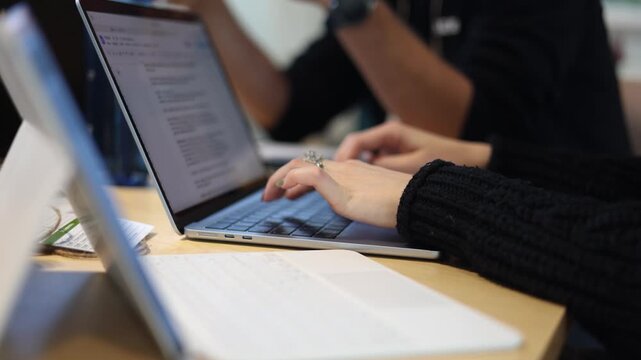 Close-up of hands typing on a laptop keyboard during a collaborative work session, with notes, documents, and colleagues contributing to a focused project
