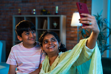 Indian Child and mother capture fun selfie on sofa, showing love and family bonding indoors