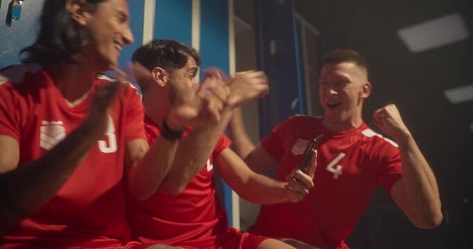 Group of Soccer Teammates Sitting Side by Side, Focused on a Mobile Phone. Suddenly They Cheer Loudly, Celebrating Victory and Expressing Excitement Over What They See on Screen or a Winning Bet