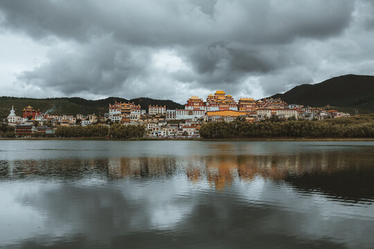 View of golden rooftops glisten above the tranquil lake reflecting the ancient monastery against a backdrop of rolling hills, Di Qing Zang Zu Zi Zhi Zhou, Yun Nan Sheng, China.