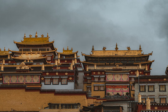 View of tiered architecture with gold roofs under a cloudy sky, showcasing intricate details in Di Qing Zang Zu Zi Zhi Zhou, Yun Nan Sheng, China.