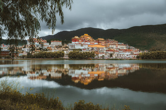 View of the golden roofs of Songzanlin Monastery shimmer in the still lake waters beneath an overcast sky, Di Qing Zang Zu Zi Zhi Zhou, Yun Nan Sheng, China.