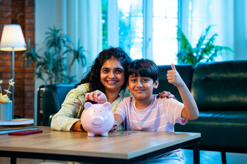 Indian Child and mother putting coins in piggy bank, sharing fun learning and family bonding