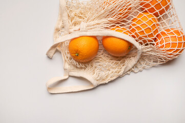 Eco-friendly thread bag for shopping, buying food, fruits, vegetables. Ripe juicy oranges in cotton string bag on gray background top view flat lay. Zero waste, plastic free concept. Citrus fruits