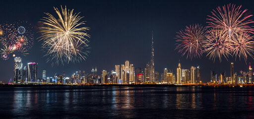 Wide panoramic night view of Dubai Downtown cityline from Dubai Creek Harbour, illuminated skyscrapers and festive fireworks lighting up the New Year sky