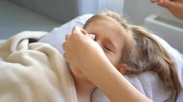 Mothers hands drips into eye eye drops of little girl and wipe with cotton pad. Eye medication. Childhood diseases. Infection cold flu illness