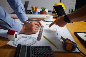 Close-up of architects measuring and drawing house plan with pencil and ruler on blueprint,...