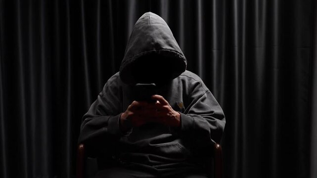 Anonymous hooded hacker using a smartphone in the dark