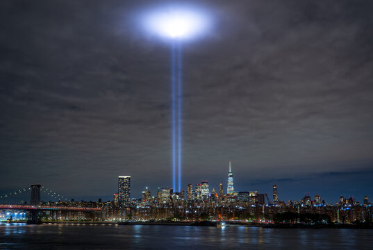 Tribute in Light. View of two powerful beams of light pierce the night sky above a glittering cityscape reflected in the dark water, a poignant tribute of 9-11, New York, New York, United States.