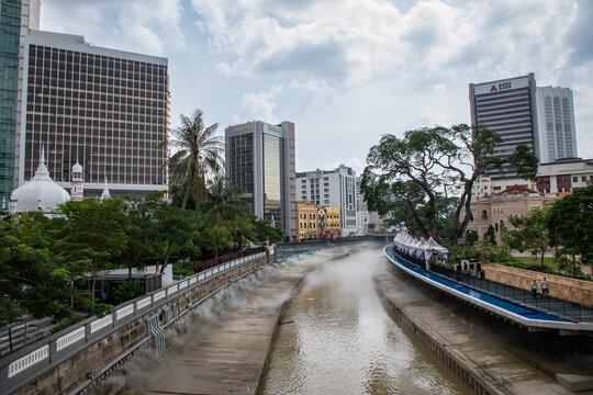 View of a river flowing through a concrete channel flanked by lush greenery and modern skyscrapers under a cloudy sky, Kuala Lumpur, Federal Territory of Kuala Lumpur, Malaysia.