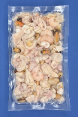 A close-up studio shot shows a clear vacuum-sealed package of mixed frozen seafood on a deep blue background