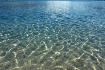 Fototapeta premium Crystal Clear Turquoise Water Revealing Sandy Bottom with Sunlit Ripples and Shadows transparent shallow