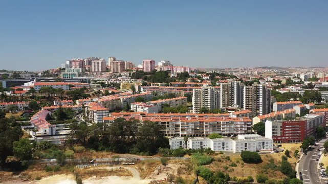 Aerial drone view of residential buildings and urban development with clear blue sky and green surroundings, highlighting modern city life in Amadora