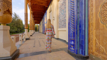 Woman in Uzbek patterned attire admiring traditional architecture in Tashkent