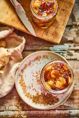Homemade apple chutney in glass jars with visible chunks of apple, pear, dried fruit, ginger, and spices. Preserved autumn condiment on a rustic wooden background, perfect for seasonal cooking.