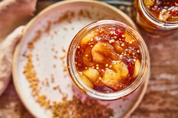Close-up of homemade apple chutney in a glass jar with chunks of apple, mustard seeds, and spices. Rustic food photography of seasonal fruit preserve.