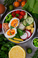 Poke bowl with smoked redfish, eggs, vegetables, edamame beans and rice served on gray table. Healthy balanced meal with white fish. Top view