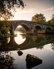 Stone bridge over tranquil river at sunrise