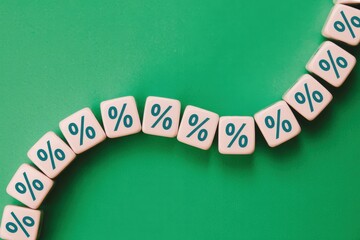 A line of percentage sign blocks curving upwards on a green background, symbolizing financial growth and increasing interest rates