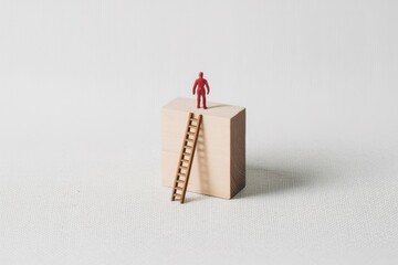 A miniature red person stands victorious on a block, having climbed a ladder, a metaphor for business success and personal growth