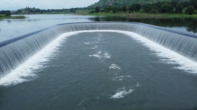 Aerial view of the Zuma Barracks dam overflow showing the curved dam wall and the cascading water flowing into the pool, Suleja, Niger, Nigeria.