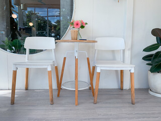 a cozy, modern cafe setting. In the center is a small, circular wooden table with striking white and light wood legs, flanked by two matching simple white chairs