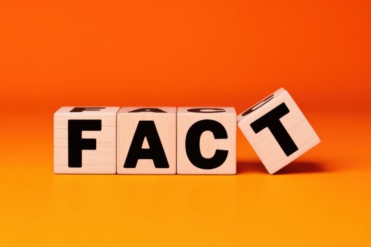 Wooden cubes with black letters spelling the word FACT, with the last block tilted, on a bright orange background symbolizing truth and evidence
