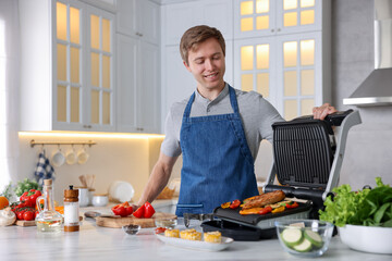 Man cooking vegetables and meat on electric grill in kitchen