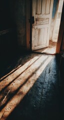 Obraz premium Sunlight streams through an antique, weathered door, casting dramatic shadows on a worn wooden floor, creating a sense of mystery and serenity.